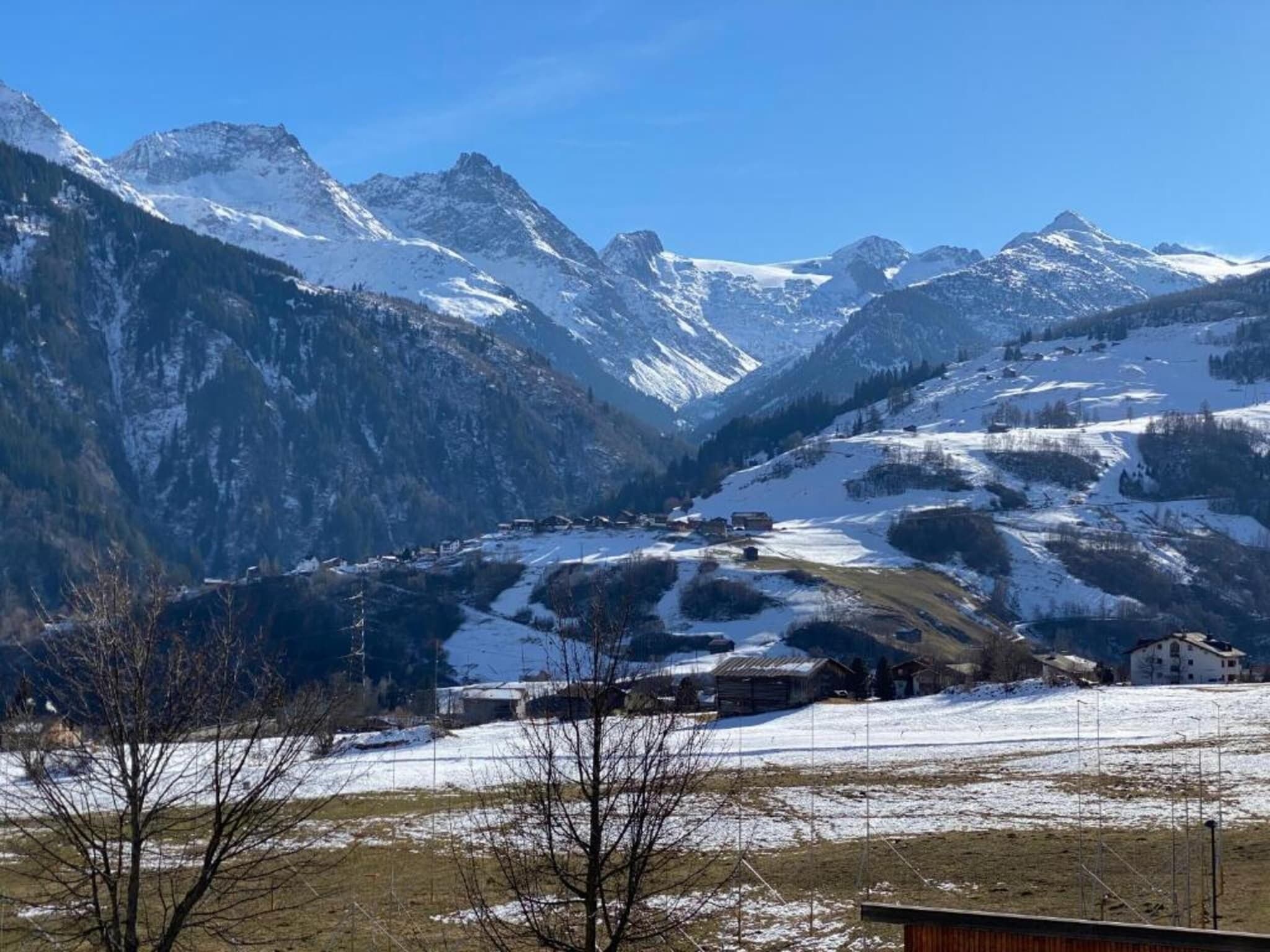 A mountainous landscape with snow-covered peaks and a valley with buildings.
