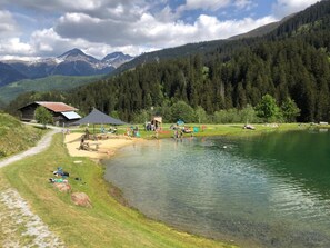 Una cabaña junto al lago con un porche y una zona cubierta, rodeada de bosque y montañas.