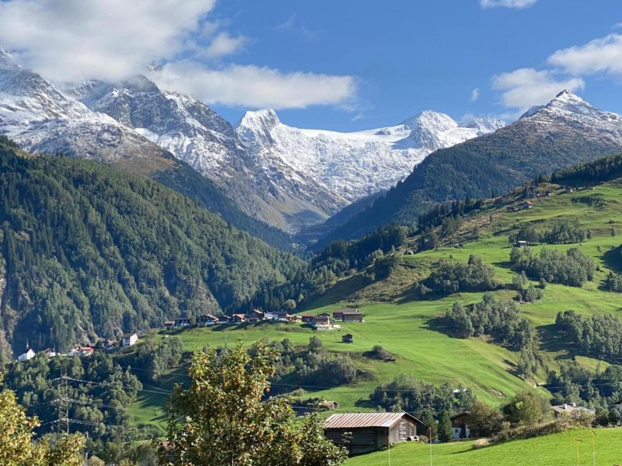 Un paysage montagneux avec une vallée, des maisons et des sommets enneigés.