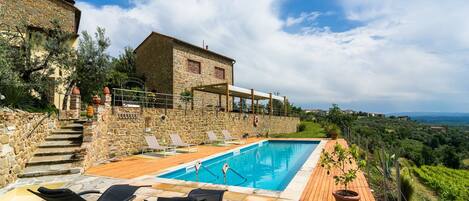 A stone building with a pool, lounge chairs, and a view of the countryside.