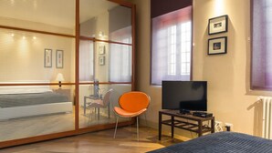 Una habitación de hotel moderna con una cama grande, televisión, una silla y una puerta corrediza de vidrio.