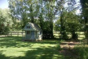 Cozy cabin with a gabled roof and a front porch, set amidst a serene grassy area.