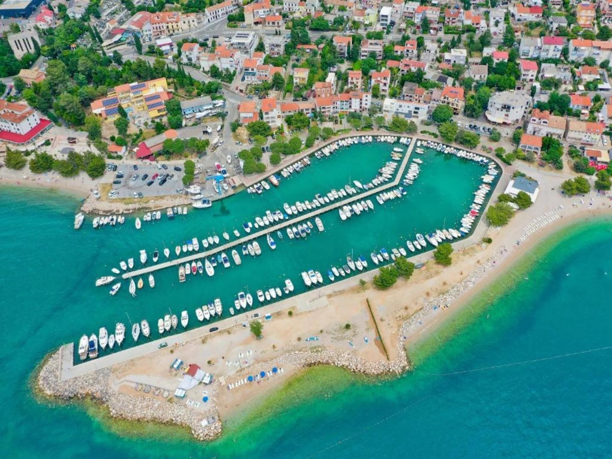 An aerial view of a coastal town with a marina, residential buildings, and a sandy beach area.