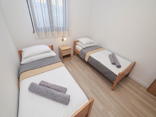 A twin room with two single beds, a bedside table with a lamp, and a window with blinds.