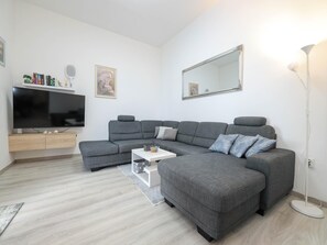 A modern living room with a grey sectional sofa, a flat-screen TV, a white coffee table, and a floor lamp.