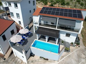 A multi-story building with a rooftop pool, solar panels, and a balcony with sun loungers.