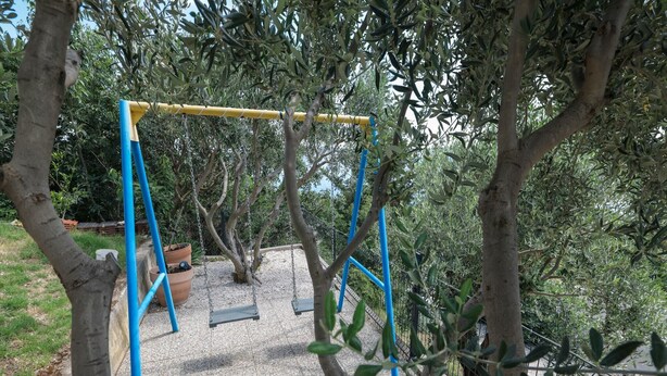 A playground with a swing set and a slide, surrounded by trees and gravel. - Luxury Apartment with heated pool in Starigrad (Starigrad)