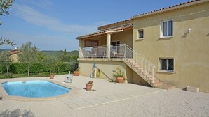 Una casa de dos pisos con piscina, mobiliario exterior y vistas a las colinas.