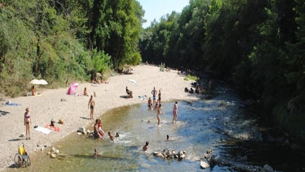 Una playa junto al río con gente nadando y tomando el sol.