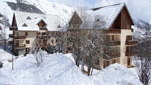 Estació d'esquí amb muntanyes cobertes de neu i edificis d'estil xalet, incloent una construcció de fusta amb un teulat pronunciat i un edifici amb terrasses i teulat pla.