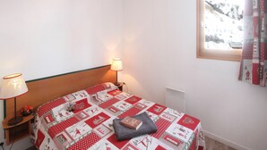 Un dormitori amb un llit, dues làmpades de nit, una finestra amb cortines i una taula petita amb un llibre.