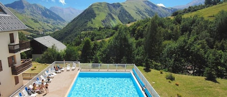 Una piscina con vistas a montañas, un edificio con balcón y sillas de descanso.