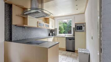 Een moderne keuken met een centraal eiland, geïntegreerde apparatuur en uitzicht op groen.