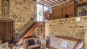 Quarto rústico com paredes de pedra, mobiliário de madeira, uma escada e uma mesa de centro de vidro.