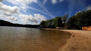 Uma praia com areal arenoso, águas calmas e árvores ao fundo.