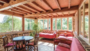 Uma cabana acolhedora com interior em madeira, uma parede de pedra, uma mesa redonda de madeira com cadeiras e um sofá vermelho.