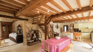 A rustic interior with exposed wooden beams, a stone fireplace, a dining area with a pink tablecloth, and a kitchen with light-colored cabinets. - Villa in Saint-Nexans with Private Heated Pool (Saint-Nexans)