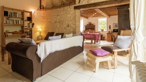 A cozy living room with a sofa, armchair, and a wooden coffee table. There is a bookshelf filled with books and a lamp on a side table. - Villa in Saint-Nexans with Private Heated Pool (Saint-Nexans)