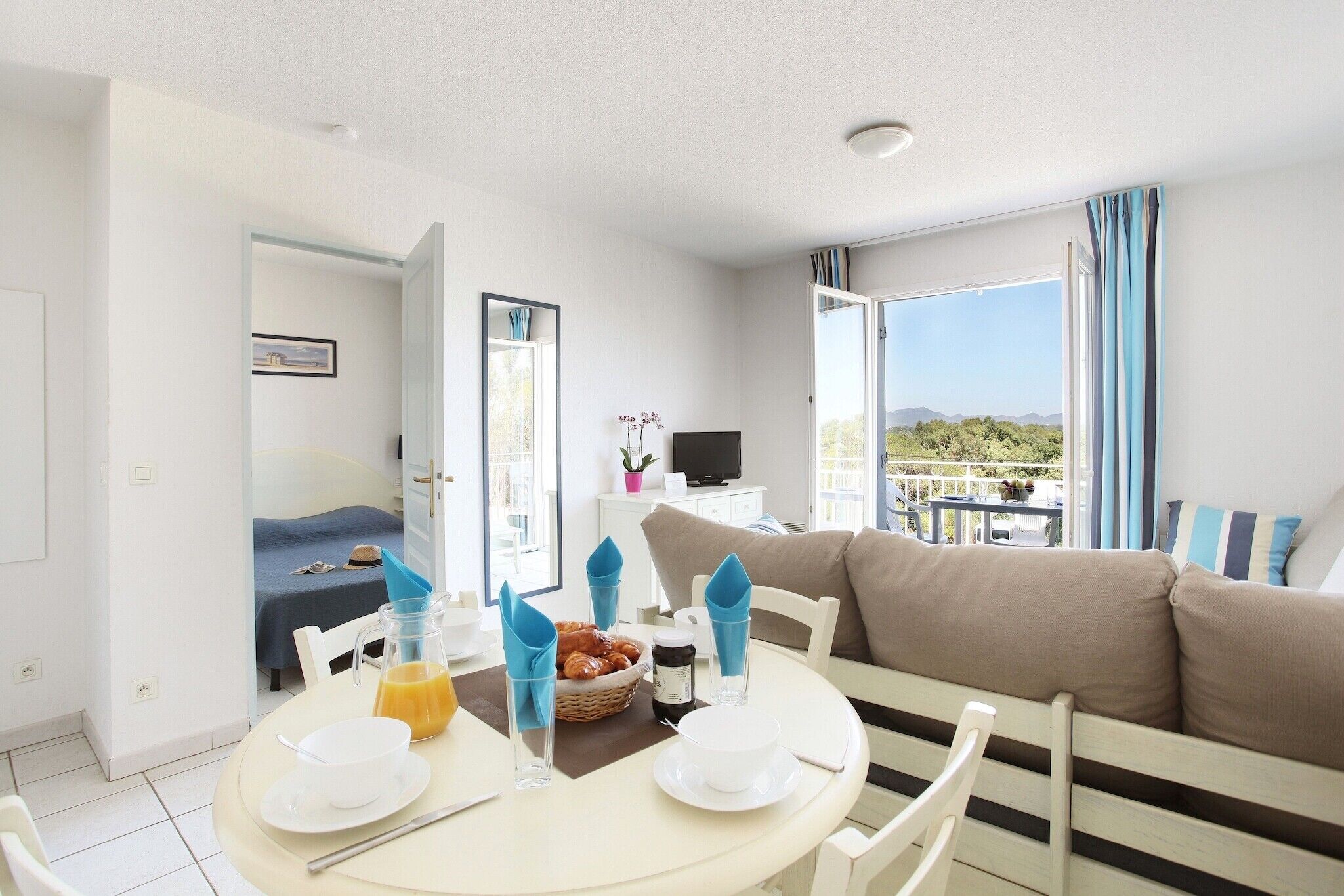 A hotel room with a dining area, a bed, a TV, and a balcony with a view.