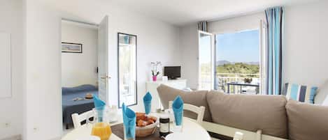 A hotel room with a dining area, a bed, a TV, and a balcony with a view.
