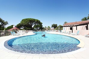 A large, clear swimming pool with lounge chairs and a palm tree in the background.