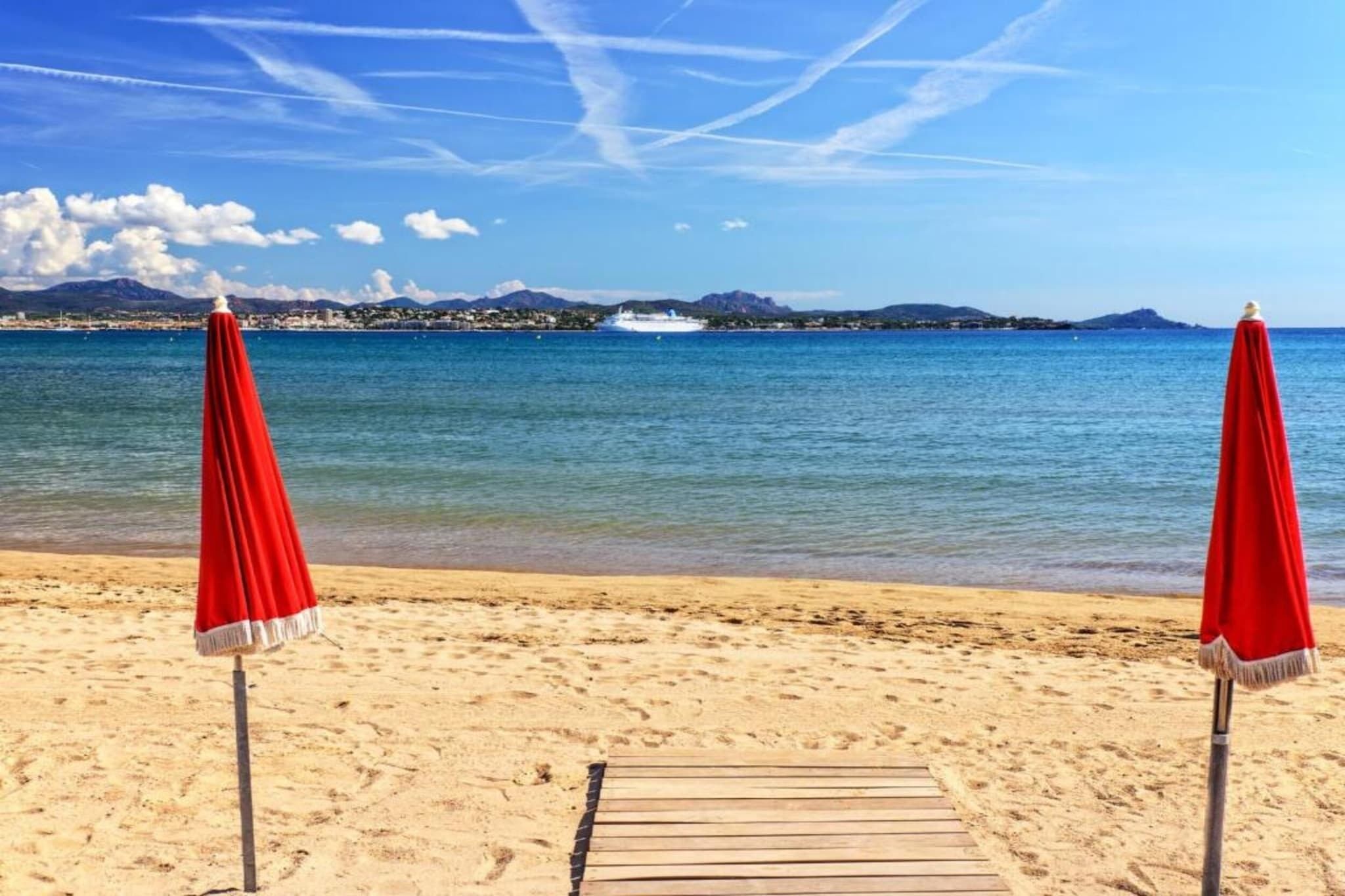 A beach with two red umbrellas and a wooden walkway leading to the water.