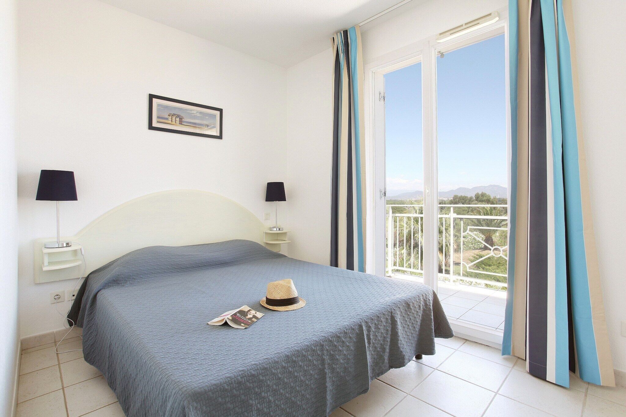 Un dormitorio con cama, dos lámparas de noche, un cuadro en la pared y vistas al exterior a través de una puerta corredera.