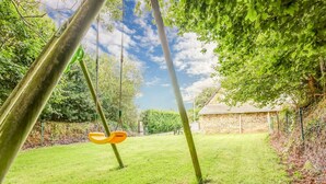 A grassy outdoor area with a swing set and a stone building in the background.
