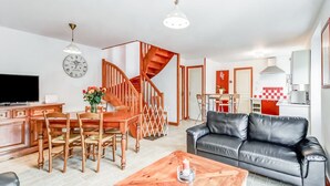 A modern living room with a wooden dining table, a black leather sofa, a wooden coffee table, and a staircase leading to an upper floor.