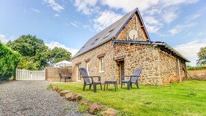 A stone building with a sloped roof, a gravel driveway, and a grassy yard with outdoor seating.