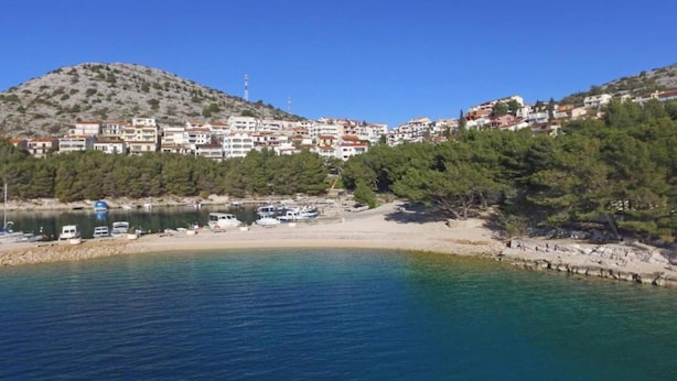 A coastal town with buildings on a hillside, a sandy beach, and boats in the water.