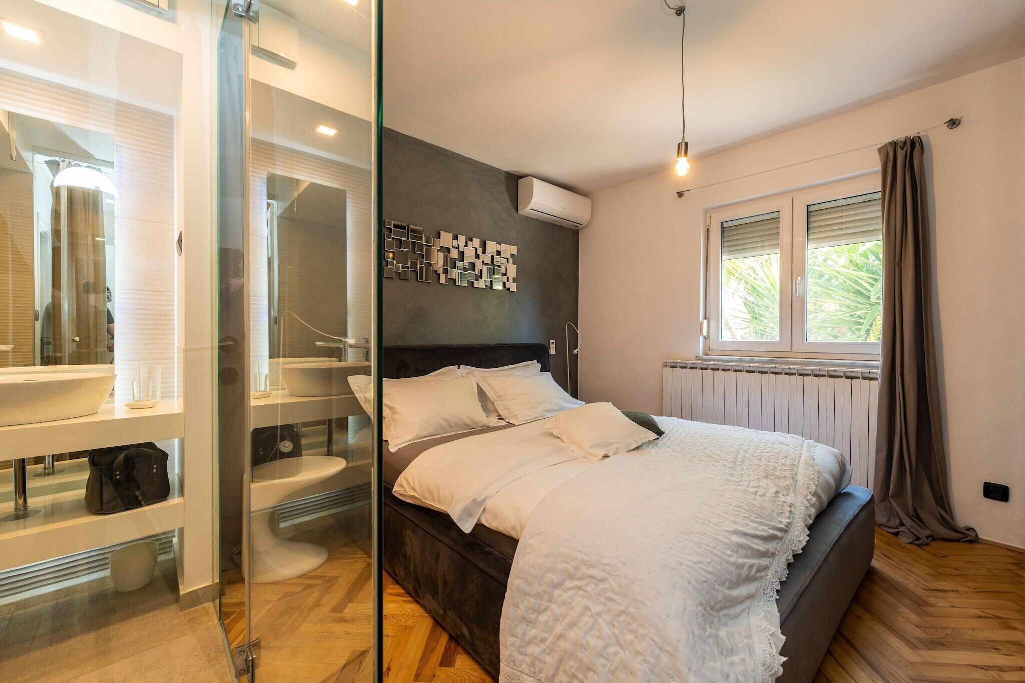 A modern bedroom with a glass shower enclosure, a bed with white bedding, and a window with curtains.