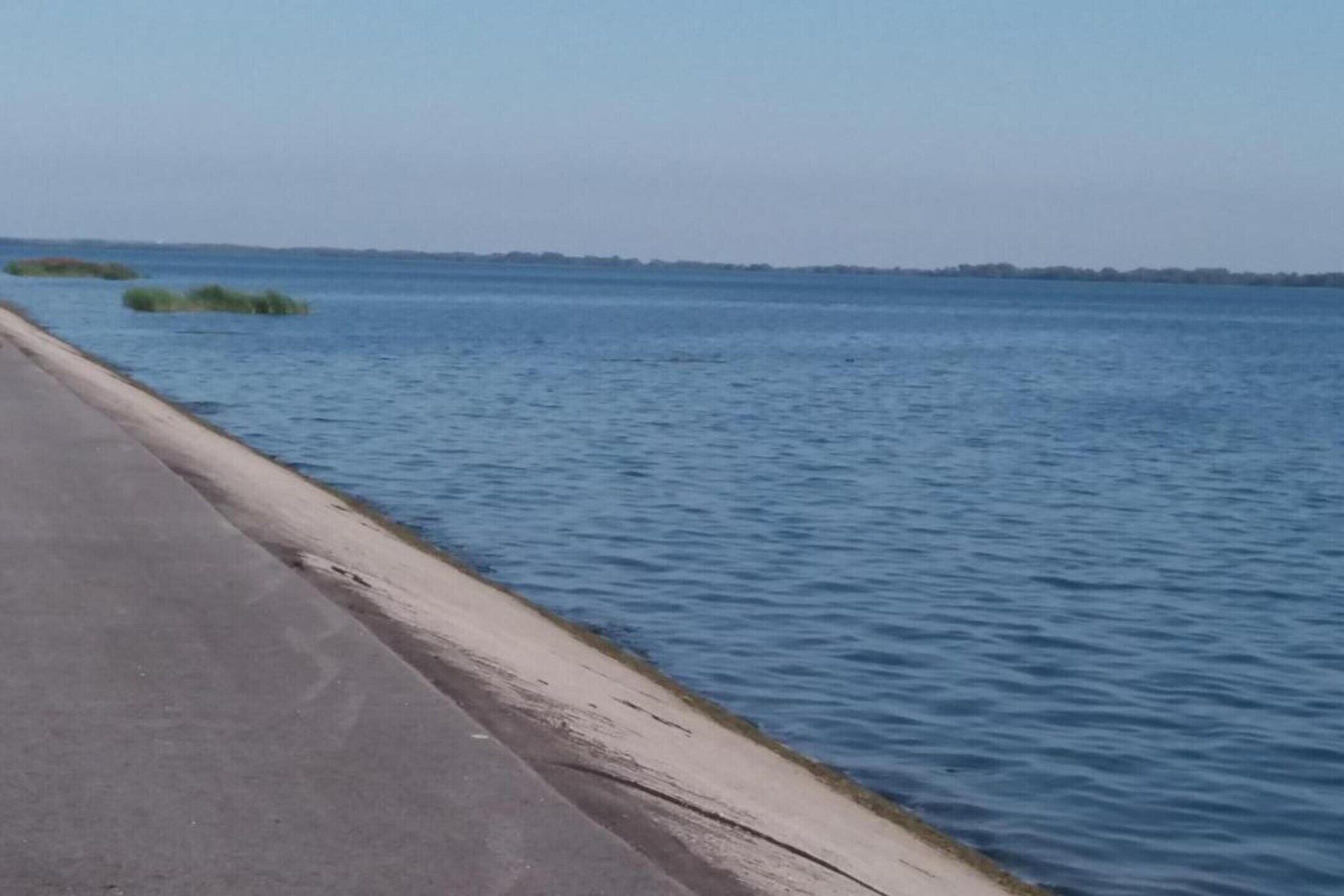 A concrete pathway alongside a calm body of water with distant land visible.