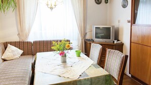 Un salon chaleureux avec un canapé, une table à manger recouverte d’une courtepointe, un téléviseur et une plante.