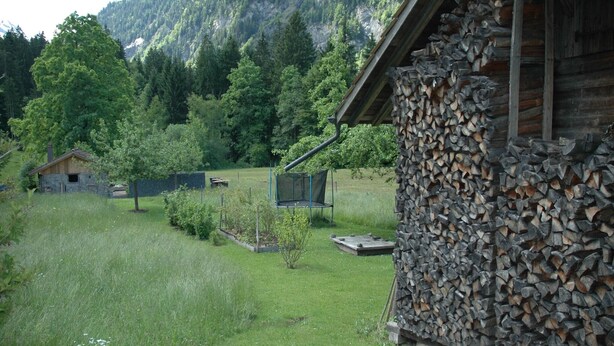A rustic cabin with a stone wall and a wooden roof, surrounded by a lush green landscape and a mountain in the background.