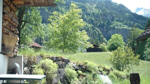 A patio with a table and chairs, a potted plant, and a view of a mountainous landscape with a house in the background.