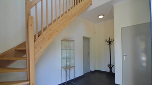 Un hall d’entrée spacieux avec un escalier en bois, une vitrine et une porte.