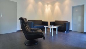 Un espace détente moderne avec un fauteuil en cuir noir, deux canapés et une petite table blanche.