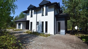 Une maison moderne à deux étages, avec une allée pavée en briques et un petit jardin.