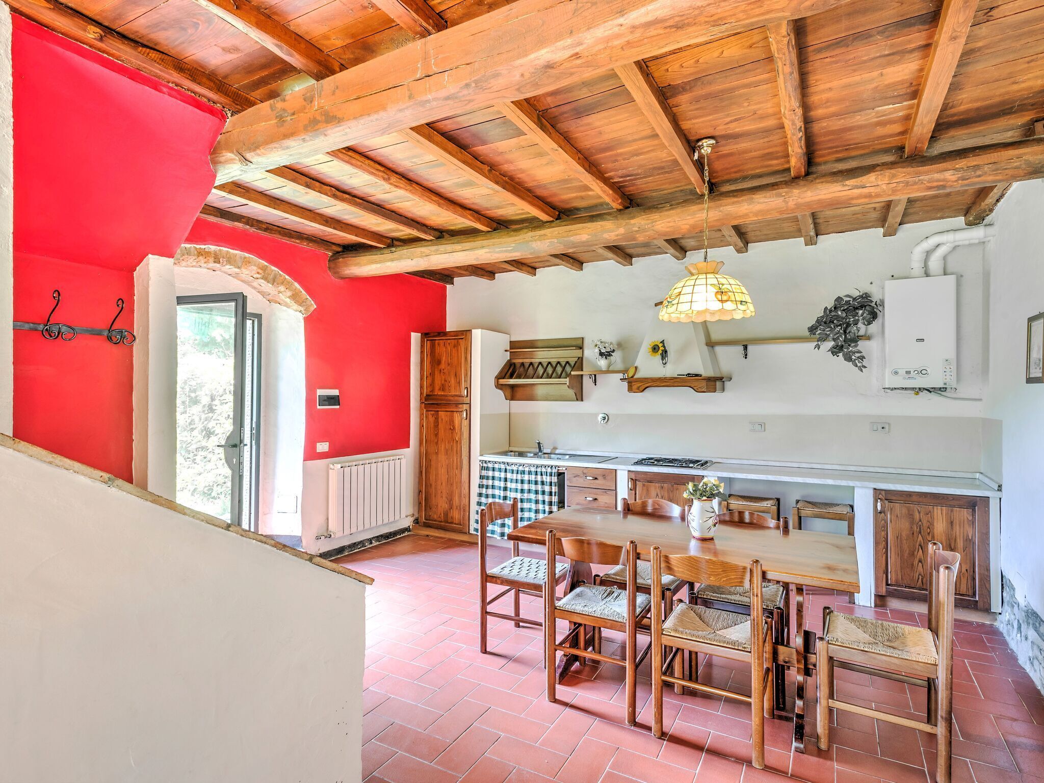 Une cuisine rustique avec un mur rouge, des poutres en bois au plafond et un sol carrelé.