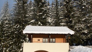 Une cabane en bois, dont le toit est recouvert de neige, entourée d’arbres chargés de neige.