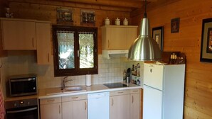 Une cuisine compacte avec des meubles en bois, un four encastré, un micro-ondes, un évier et un luminaire suspendu en acier inoxydable.