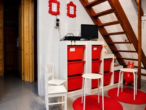 A room with a white chair, red storage bins, a television, and a wooden ladder. - Holiday Home in Ardennes near Hotton Caves (La Roche)