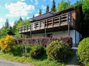 A two-story building with a balcony, surrounded by greenery and trees.