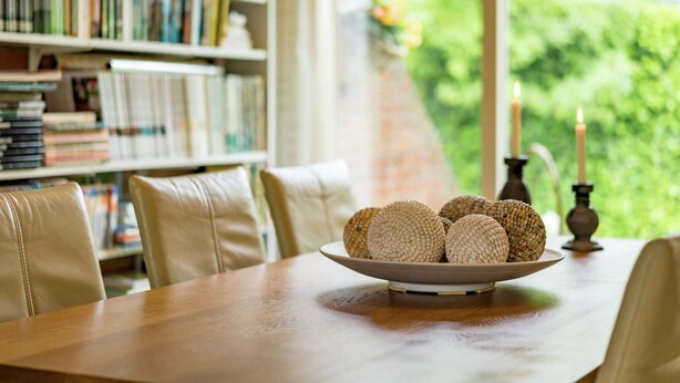 A dining table with a bowl of round, textured cookies, a candle holder with candles, and a bookshelf filled with books.