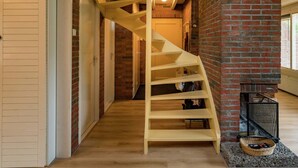 A wooden spiral staircase in a hallway with brick walls and a fireplace.