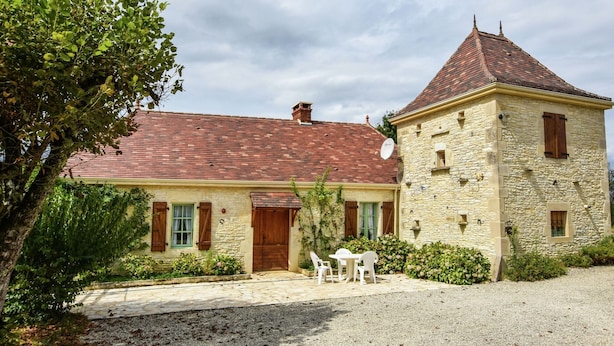 A stone building with a red-tiled roof, a wooden door, and a small garden area with a table and chairs.
