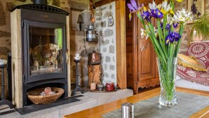 Een rustiek interieur met een stenen muur, een houten tafel, een vaas met bloemen en een traditionele houtkachel.