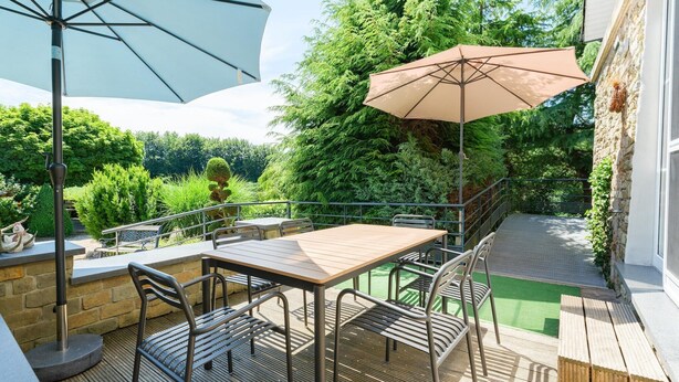 Een terras met een tafel, stoelen, twee parasols en een stenen muur.
