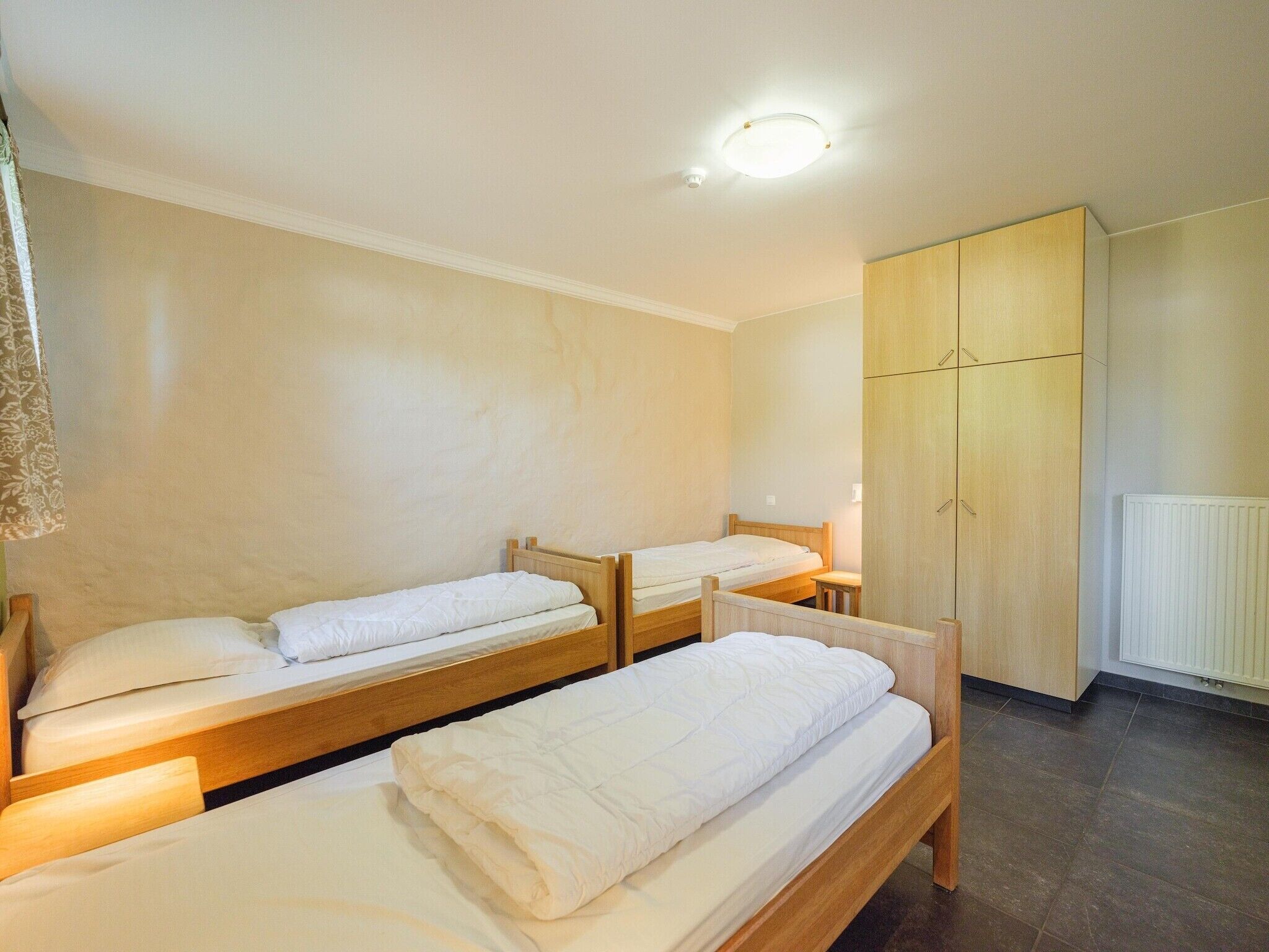 Ein Hotelzimmer mit drei hölzernen Betten, einem Kleiderschrank und einem Heizkörper.